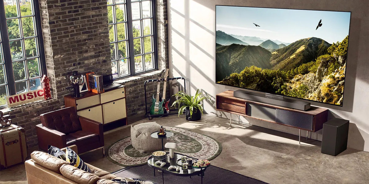 LG OLED TV displaying wooded mountain sign on a TV stand in a modern sunlit living room