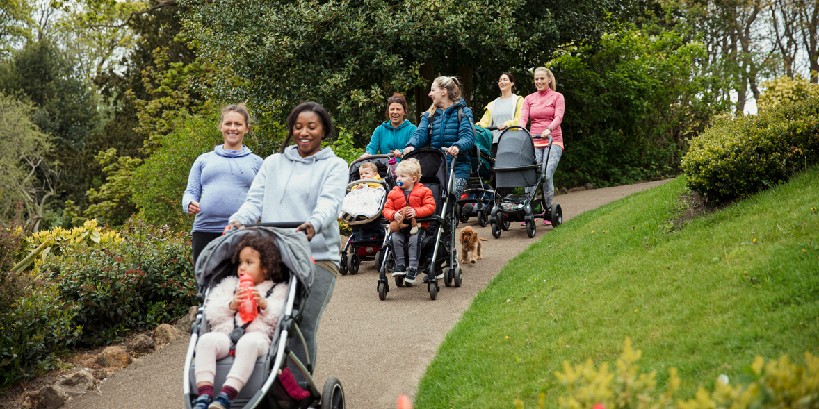 Five mothers with five children in pushchairs and a pregnant woman walking in a park