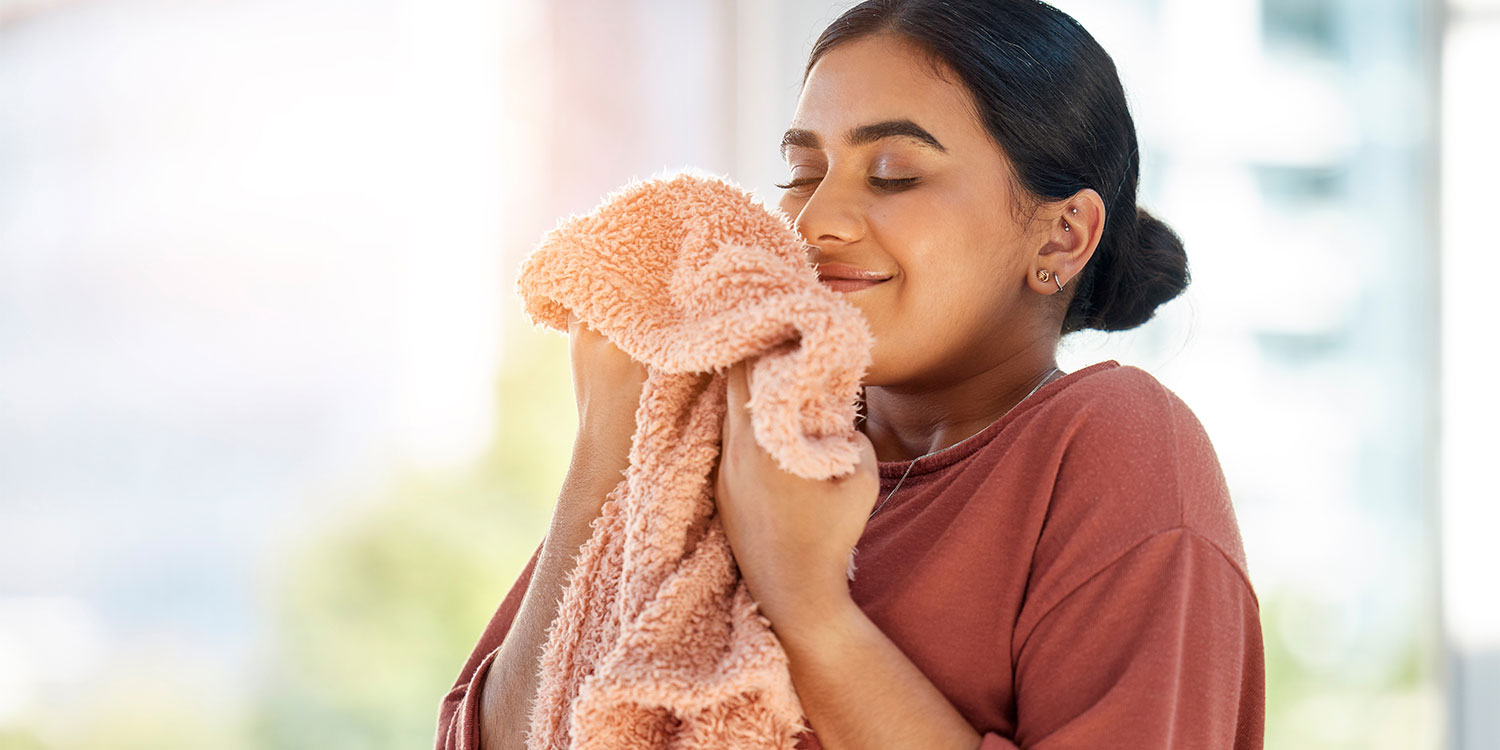 Young woman looking delighted as she hugs a peach-coloured fluffy towel and inhales its fresh smell
