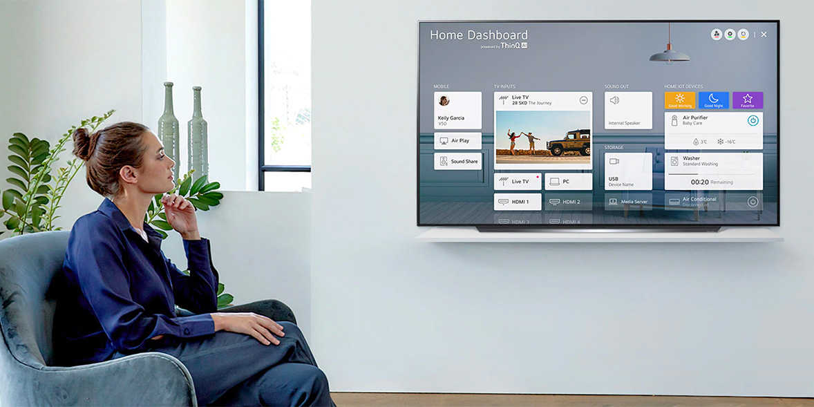 A woman watches a 4K OLED TV mounted on a white shelf. It is displaying the smart home screen